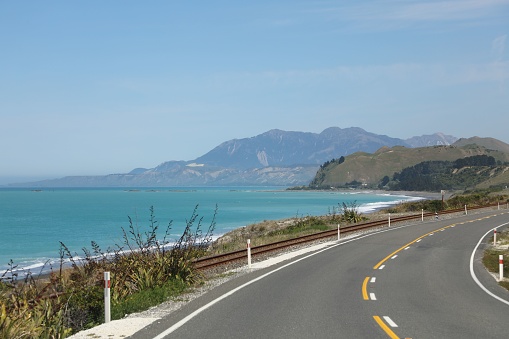 A scenic view of an empty winding road on the side of a mountain with the backdrop of the ocean