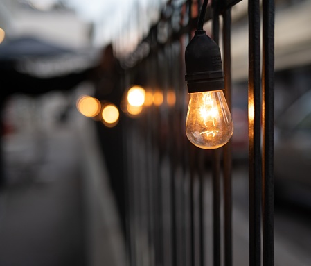 An image of a row of lightbulbs illuminated against a fence in a residential area at dusk