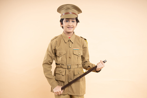 Young elementary indian boy kid wearing police uniform showing with his nightstick in hand isolated on beige studio background. Closeup