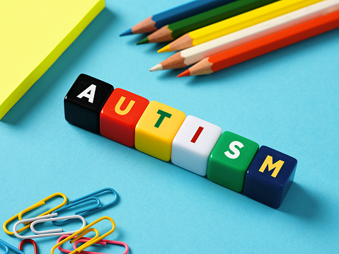 Autism and education concept. Autism spectrum disorder. The word autism on colorful cubes with stationery objects on blue background.