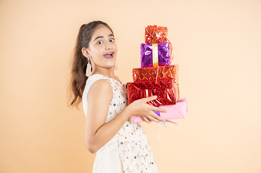 Happy beautiful indian girl wearing traditional outfit holding red gift boxes celebrating diwali festival isolated on studio background. surprise expression