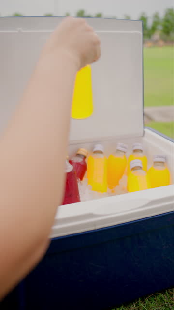 A human hand opening the ice bucket and picking up only yellow glass bottle for recovering himself after practicing in the soccer field