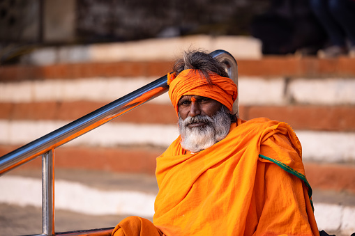 Varanasi, Uttar Pradesh, India - November 2022: Portrait of Unidentified Indian sadhu baba in traditional clothes sitting on ghat near river ganges in varanasi city.
