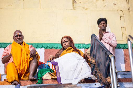 Varanasi, Uttar Pradesh, India - November 2022: Portrait of Unidentified Indian sadhu male and female in traditional clothes sitting on ghat near river ganges in varanasi city.