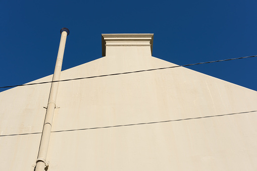 Close-up on a side wall of a building with chimney and deep blue sky beyond.