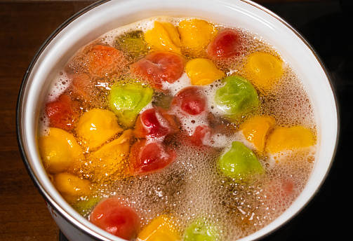 Multi-colored Pelmeni dumplings are boiled in water in an iron pan, food preparation process