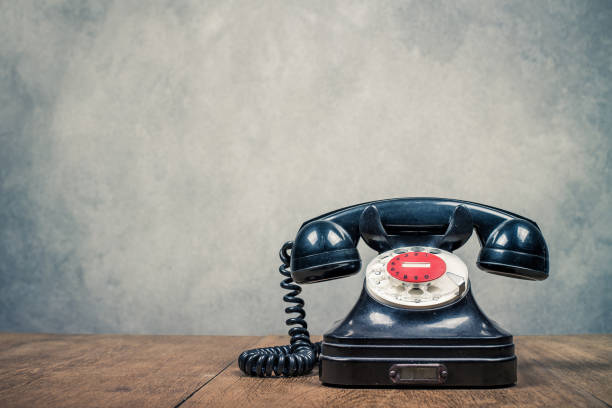 istock Retro old black rotary telephone on table front textured concrete wall background. Vintage style filtered photo 1501489584