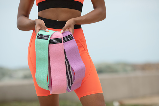 Cropped shot of young toned slim woman holding a fitness elastic resistance band.