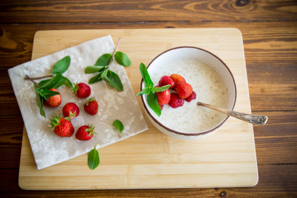 cooked diet oatmeal in a bowl with fresh ripe strawberries, on a wooden table.