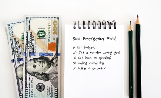 Dollars cash money, pencils and notebook with text written BUILD EMERGENCY FUND , concept of setting and planning financial goal to save money for emergency