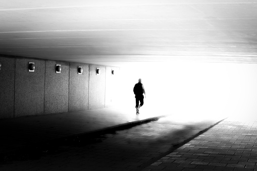 Unrecognizable silhouette of man in motion blur walking in to the light in black and white