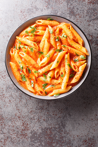 Delicious beautiful prepared bowl of penne pasta in pink tomato sauce closeup on the bowl on the table. Vertical top view from above