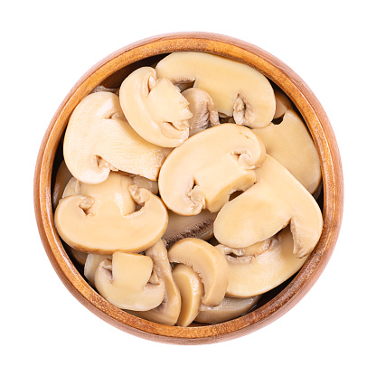 Canned sliced white champignon mushrooms, in a wooden bowl. Agaricus bisporus, also called common, button, cultivated or table mushroom. Close-up from above, isolated on white background, food photo.