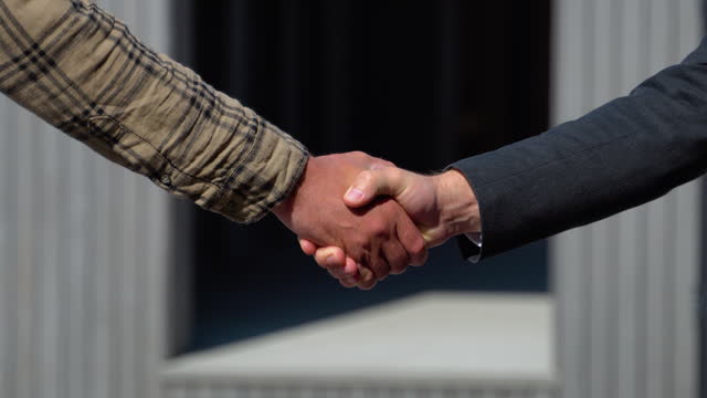 Real estate agent gives the keys to client and shaking hands after the sale of a modular house. The homeowner is happy after receiving the transfer of the right to occupy the prefabricated home