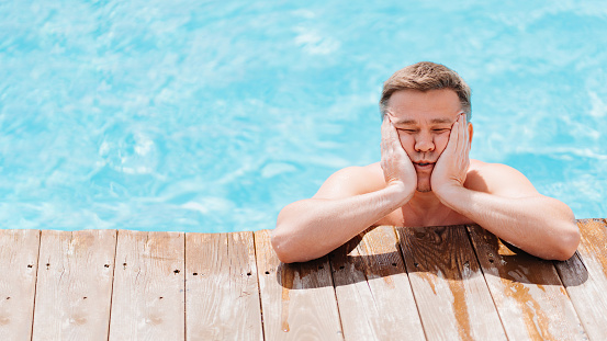 Portrait of a sad and dreamy middle-aged man in the pool at the side. The concept of summer recreation by the water and the construction of swimming pools in hotels and houses