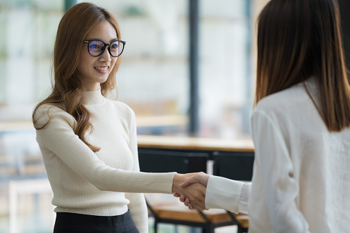 A pretty Asian businesswoman shaking hands with a businesswoman in her office during a meeting.