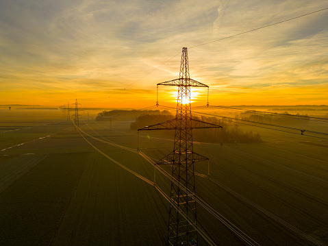 High voltage electricity power pylon tower on agricultural field during sunset