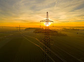 High voltage power pylon on agricultural field during sunset