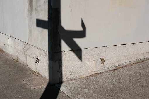 Shadow from a damaged street sign on an old white wall.