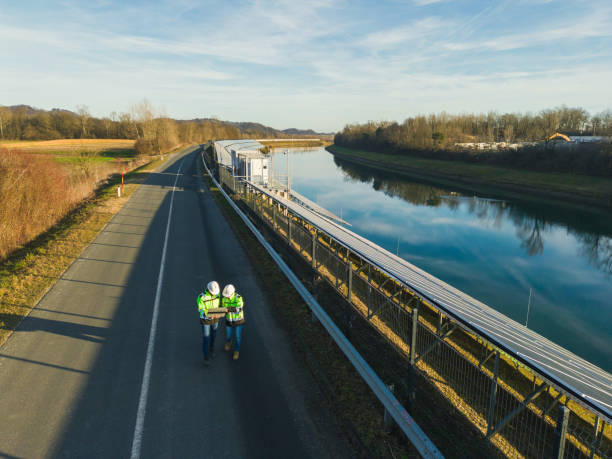 AERIAL VIEW  Two engineers using laptop next to solar power plant by river