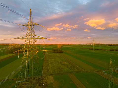 High voltage lines and pylons on a green agricultural landscape under cloudy sky