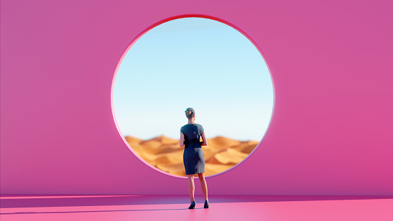 Woman stands in front of pink wall with a hole. She looks towards the horizon. It is sunny and in the background is a desert. The scene is tranquil.