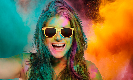 Carefree cheerful woman covered in rainbow colored powder celebrating the festival of colors. Young woman having fun with colorful holi powder.