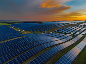 Solar panels on agricultural field during sunset. Aerial view of solar energy panels rows along the agriculture field. Photovoltaic pv plant from drone point of view. Alternative power energy concept.