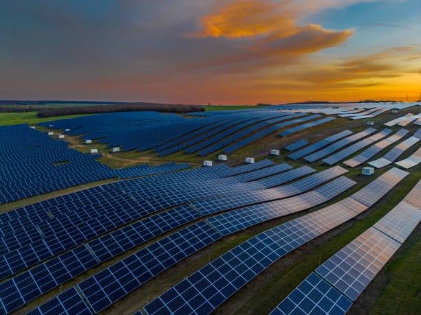 Solar panels on agricultural field during sunset. Aerial view of solar energy panels rows along the agriculture field. Photovoltaic pv plant from drone point of view. Alternative power energy concept. stock photo
