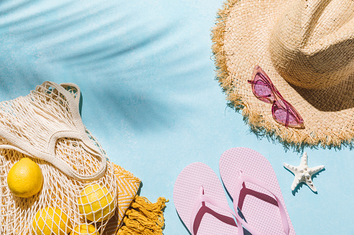 Summer flat lay with sunglasses, straw hat and beach accessories on blue background with palm leaf shadow, sun and sunlight. Vacation, holiday, summer creative concept, copy space, top view