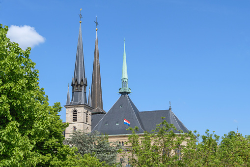 Luxembourg city - Luxembourg 06-05-2023. Fragment of the main cathedral of Luxembourg. The spiers of the towers of the central cathedral against the backdrop of a bright spring sky and fresh foliage of trees.