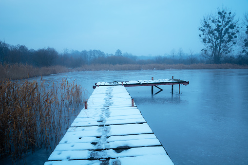 Snow on a wooden pier on the lake shore, view on a foggy December day, Stankow, Poland