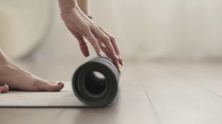 Close up shot of young adult Caucasian female unrolling yoga mat before yoga practice at home.