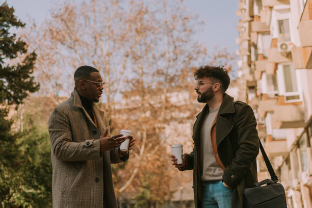 istock Young black male programmer explaining to his white colleague how to fix the error at the code while walking out in the city and having a coffee time, after work 1501727837