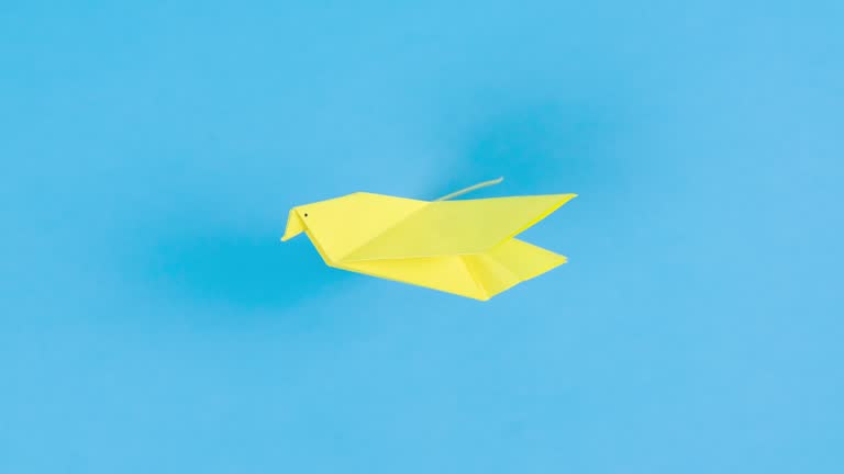 Yellow paper origami dove flies flapping its wings. Blue background. Symbol of peace.