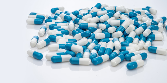 Blue-white antibiotic capsule pills on white background. Pile of antibiotic drug. Antibiotic drug resistance. Prescription drugs. Healthcare and medicine. Pharmaceutical industry. Pharmacy product.