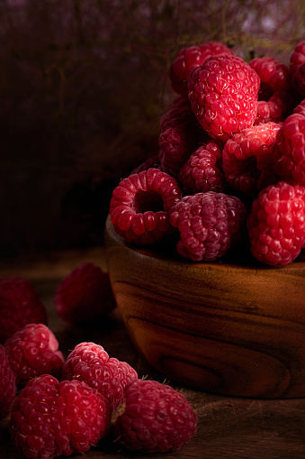 Photo a red raspberries in a wooden bowl on wooden board background with blurred background.