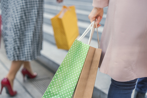 Two women holding shopping bags and walking up the stairs outdoors in city