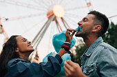 Laughing girlfriend feeding her boyfriend with cotton candy. Young couple having fun in amusement park eat cotton candy.