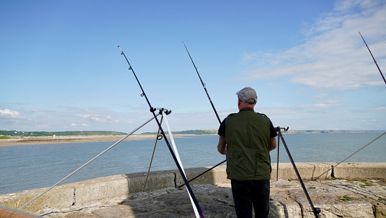 Porthcawl, Bridgend, Wales - June 20 2023: Fishermen young and old enjoy sea fishing and cast their rods into the sea-water from the tight space around the Porthcawl Lighthouse.