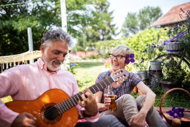 Elderly couple playing guitar and singing while sitting on the grass. They are having a picnic and are making memories