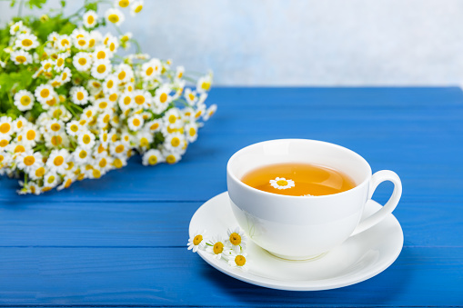 Chamomile tea in a cup on a blue textured background. Natural hour with chamomile flowers. Herbal tea. Immunity tea.Natural healer concept. Healthy detox drink.Close up. Place for text.