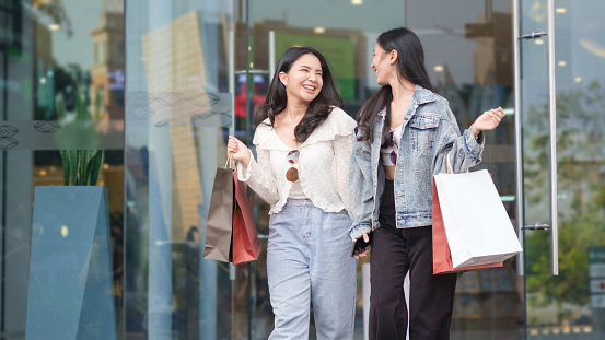 Joyful young woman carrying shopping bags walking out from shop and laughing, enjoying sales weekend.
