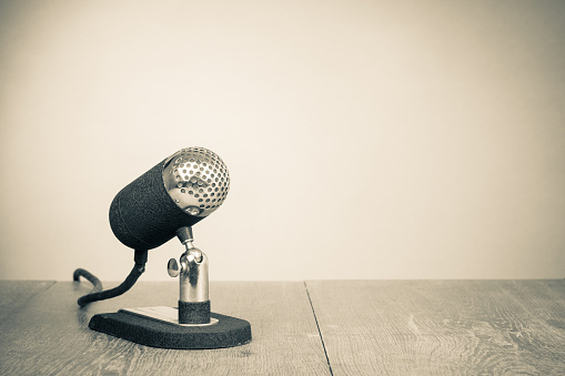 Old retro microphone from 50s on wooden desk. Vintage style sepia photo