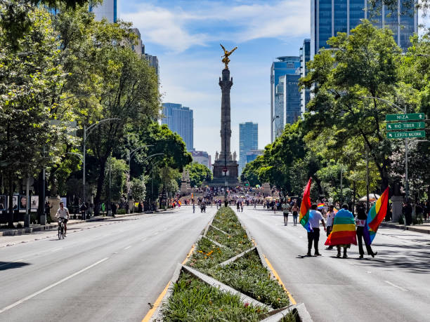Mexico City, Mexico - June 24th, 2023. Participants with rainbow flags arriving at the Pride Parade in Mexico City, with the Independence Angel monument in the background