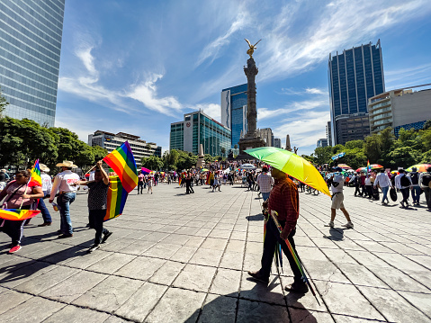Mexico City, Mexico - June 24th, 2023. People selling rainbow flags and umbrellas prior to the Pride Parade in Mexico City, with the Independence Angel monument in the background