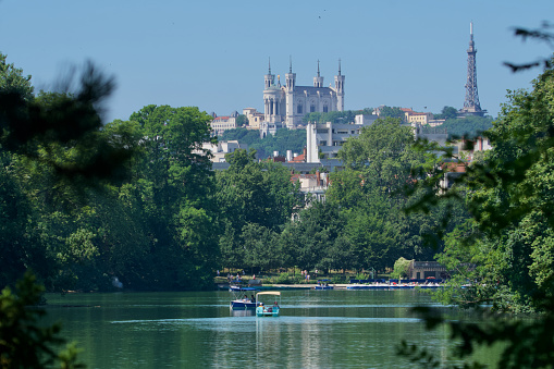 View of the Basilica of Our Lady of Fourvière through the trees with the lake of the golden head park (parc de la tête d'or) in the foreground in Lyon, France.
