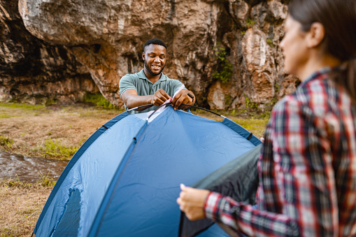 Happy multiracial couple taking apart the tent in nature
