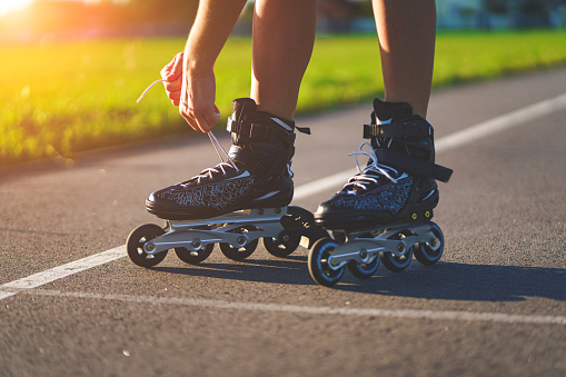 Woman laces roller skating for inline skating. Teenager rollerblading outdoors