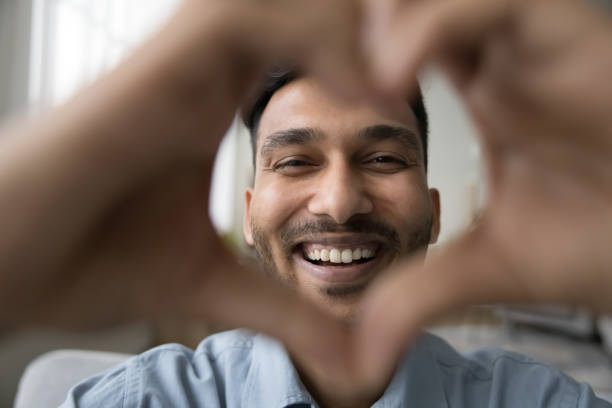 jeune indien joyeux souriant à la caméra à travers le cœur de la main - looking at camera facial expression gesturing touching photos et images de collection